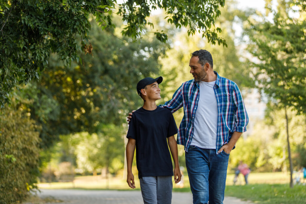 Front view of father and son walking embraced at the park, chatting and bonding