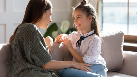 Happy young Caucasian mother and teen daughter sit relax on sofa talking sharing secrets. Smiling mom or nanny and teenage girl child rest on couch speak enjoy family weekend bonding at home.
