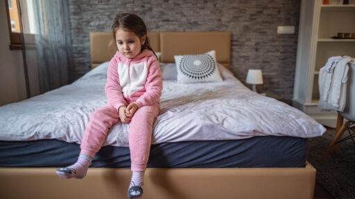 Bored child in pajamas sitting on a side of a bed