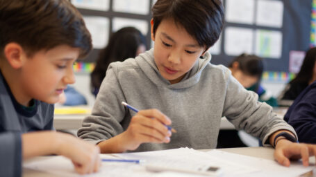 Asian multiracial Korean Japanese boy studies in elementary school classroom with classmate