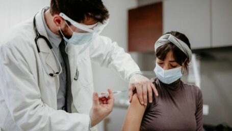 A medical professional gives a third dose of the COVID vaccine to a young woman.