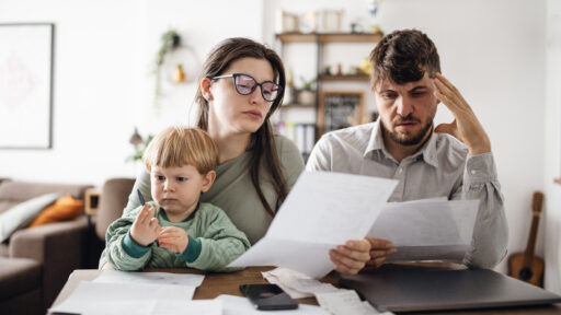 Young family of three with a toddler managing their budget, paying bills and taxes online and calculating monthly expenses at home.