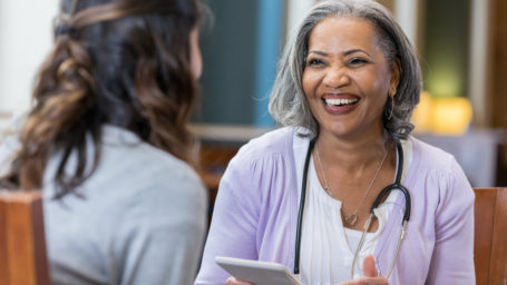 African American female medical school professor talks with female student. The professor is holding a digital tablet.