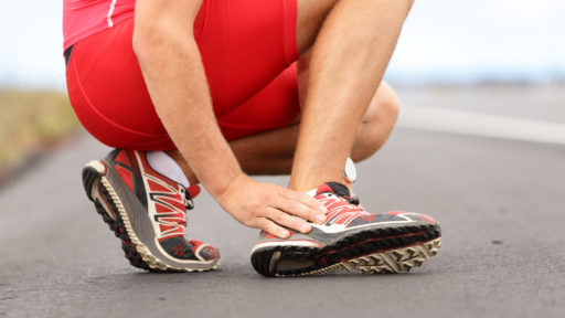 Male runner touching foot in pain due to sprained ankle.