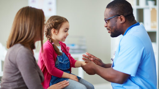 Image of a male doctor examining a young girl as her mother sits nearby.