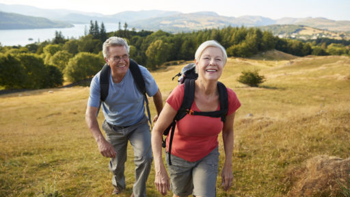 Senior Couple Climbing Hill On Hike Through Countryside