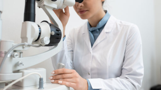 Young female ophthalmologist in whitecoat using new medical equipment to check up eyesight of one of clients in contemporary clinics