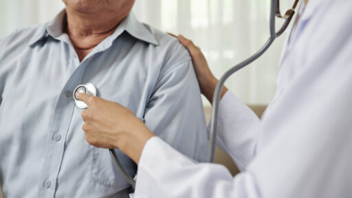Close-up of female doctor in white coat listening to breathe of senior man during his visit at hospital