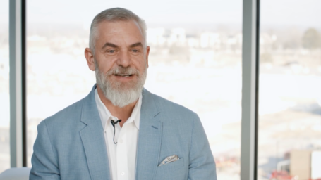 Dr. W. Cody Grammer in a light blue blazer and white shirt speaking on camera in a bright, modern medical office setting with large windows in the background.