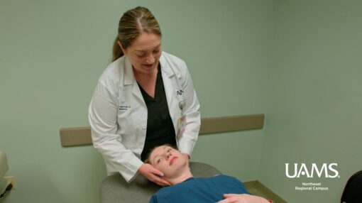 Physician at UAMS Northeast in Jonesboro examines a patient on an exam table while holding the patient's head.