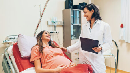 Image of a pregnant woman lying down on a hospital bed and talking to a doctor.