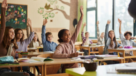 Kids in a classroom raising thier hands